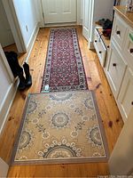 Photo showing the carpet runner extending down a hallway on wooden floor with some visible fringe and a square mat placed at the near end