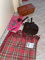 Full overview photograph showing the tartan throw, leather sporran with tassels, leather keepsake box, and jewelry arranged on a carpet.