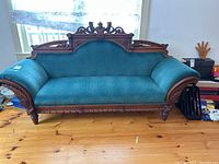 Front view of teal moire fabric settee with carved wood details on backrest and base.