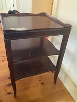 Side view of the dark wood square side table showing two shelves and tapered legs, highlighting overall wear.
