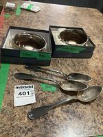 Two oval sterling silver 925 wine bottle coasters displayed in black boxes with green labels and three 800 silver serving spoons labeled Krischer.