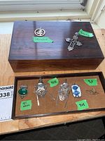 Photo showing wood jewelry box with circular stamped pendant and sterling silver cross pendant on top; jewelry box lid closed and additional earrings and pins inside box.
