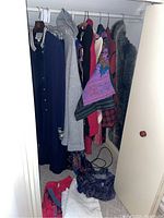 Closet view of hanging clothing items including shawls, dresses, jackets, sweaters, skirts, and scarves.