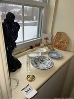 Overview of lot on windowsill showing Wedgwood dish, Thomas Hardy bowl, Limoges dish, Royal Worcester dish, black figurine statue, medicine bottles, drum beater, mesh shoe accessory, and pendant.