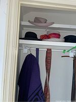 Four brimmed hats on a shelf including two black hats, one lavender hat, and one white hat with a red ribbon.