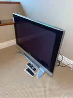 Front and side angled view of 42 inch Panasonic TV with two remote controls placed in front on the carpeted floor.