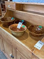 Four Bennington pottery bowls displayed on a wooden cabinet, showing various sizes and mottled brown glaze finish.