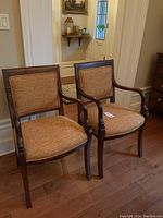 Pair of two wood frame armchairs side by side against wall, showing overall appearance and size.