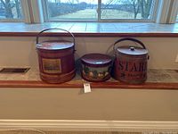Three wooden cheese boxes arranged on a stone ledge in front of a window