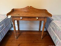 Front view of the wooden desk showing two drawers with white knobs and shaped back and side borders.