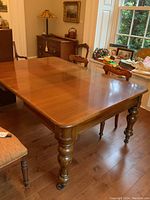 Wide shot of the full wooden dining table in a dining room, showing the table surface, leaf extension, and chairs around it.