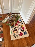 Photo showing the two hooked rugs on a wooden floor, one rolled partly, revealing detailed patterns