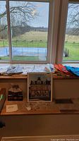 Overview of all items including shirts displayed spread on windowsill with framed print and pins on bench below