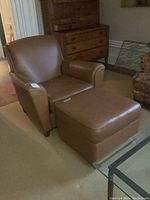Quarter front view of brown leather club armchair with matching ottoman on carpet