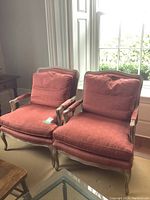 Two matching French Bergere style armchairs upholstered in rust-colored fabric placed in front of a window.