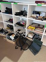 Wide view showing shelves with various cash boxes, pens, cords, binders, and other office supplies along with items in a box and on the floor.