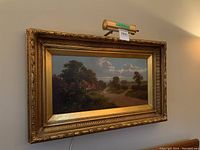 Frontal view of the framed oil painting with overhead light attached