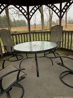 Overview of round glass top table and four swivel chairs on porch under gazebo