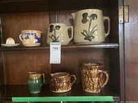Overview of six pottery pieces displayed on shelf – juicer, two brown pitchers, green creamer, two beige jugs