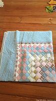 Folded patchwork quilt showing multicolor diamond pattern on one side and light blue reverse with quilting details.
