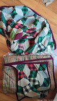 Two flannel quilts and a matching bag folded on wooden floor, showing colorful tumbling blocks patchwork pattern with purple border.