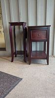Photo showing two small dark reddish-brown wooden side tables side-by-side, one with a single drawer the other with curved legs and decorative top