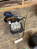 Full lot overview showing crate of golf balls, hockey stick, tennis and badminton racquets