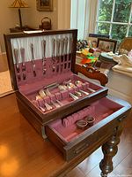 Open wooden canteen with velvet lining showing two tiers of Birks sterling flatware and napkin rings