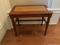 Full frontal view of wooden table showing rattan inset top and turned legs.