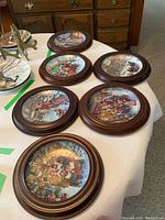 Six wooden framed collector plates arranged on table, showing various vintage style illustrations.
