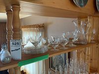 Wide shelf view showing the pitcher, footed bowls, dessert plates, and wine glasses arranged on a wooden shelf.