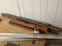 Two wood and metal levelers with two aluminum cutting guides on a wooden surface near a wood-paneled wall.