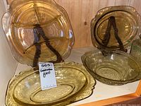 Photo showing two amber Depression glass serving trays with embossed floral and geometric patterns and scalloped edges, displayed upright on stands.