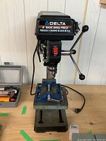Front view of Delta drill press with vise mounted on wooden bench.