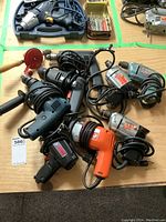 Top view of assorted electric drills on table including various brands and colors with tangled cords.