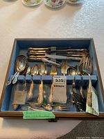 Top-down photo of the silverplate flatware arranged in blue felt-lined compartments of the wooden storage box including forks, knives and spoons in the Silver Mist pattern.