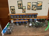 Photo of assorted nails, screws, drywall plugs, PVC clamps in jars and bottles on wood surface with decorative wood mouldings displayed on pegboard above.