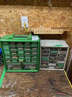 Photo of two hardware cabinets placed on a workbench against wooden wall, showing many labeled small drawers.