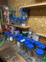 Overview photo of wooden shelves with multiple clear jars containing screws, door handles, and other hardware items.