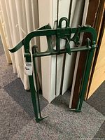 Green metal hay tongs hanging against a wall, showing full front view and shape.