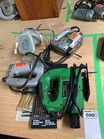 Photo showing the Superior green jigsaw, Black & Decker silver jigsaw, breathing mask, and pack of replacement blades arranged on a wooden surface.