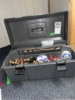 Open gray plastic toolbox filled with assorted plumbing fittings, valves, solder spool, pipe cutter, pipe sections, and clamps.