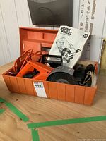 Orange Work Wheel power stripper and sander in orange plastic case with owner's manual displayed behind it.