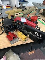 Overview of four sanders including Skil belt sander, Black and Decker, Makita, and red palm sander along with sanding blocks.