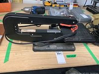 Side angle of the black Sears Craftsman scroll saw showing the arm, base, safety lever, and power cord on a wooden table.