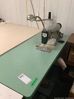 Full view of green laminated table with mounted Juki sewing machine, lamp and thread stand