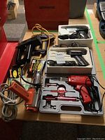 Wide photo showing various soldering guns, a heat tool, staplers, and staple boxes on a table.
