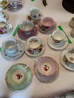 Top view of nine vintage teacups with matching saucers, assorted floral patterns, displayed on a white embossed tablecloth.
