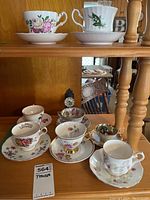 Eight vintage teacups with saucers displayed on wood shelves showing various floral and decorative patterns to illustrate the lot contents and condition.