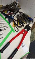 Overview of assorted hand tools spread on table including bolt cutters, pliers, crow bar, and others.